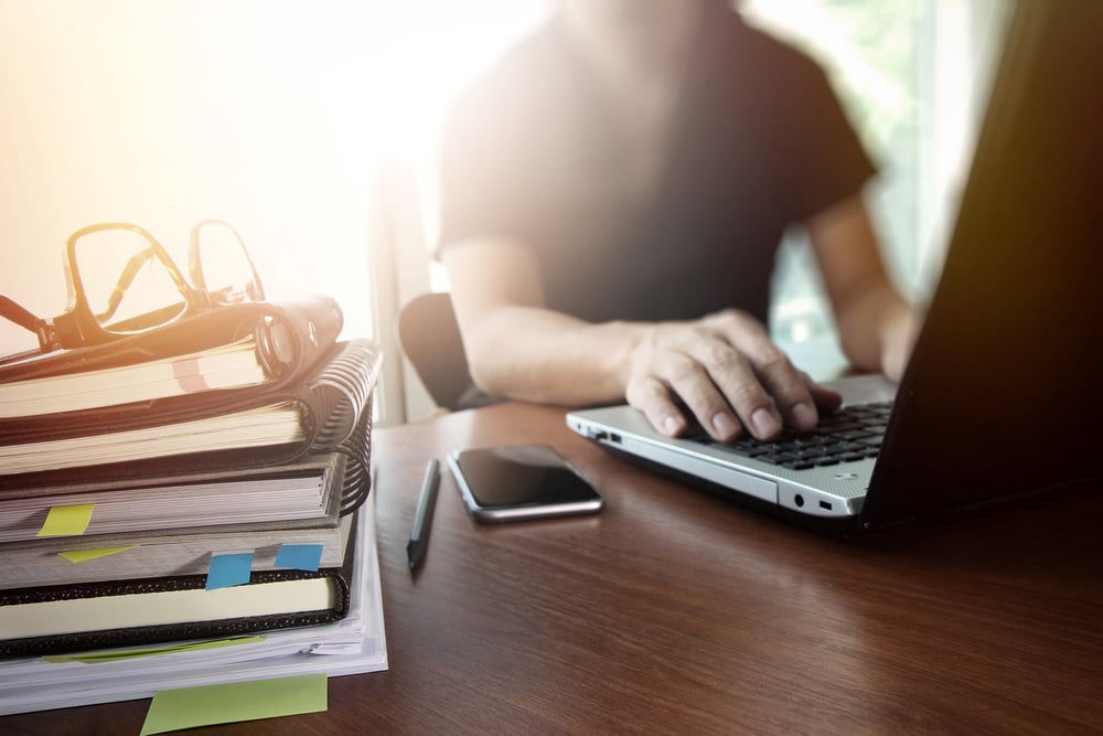 man sitting in front of computer with stack of books